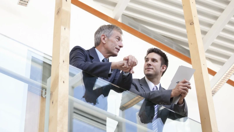 Two men in suits talking beside a glass railing