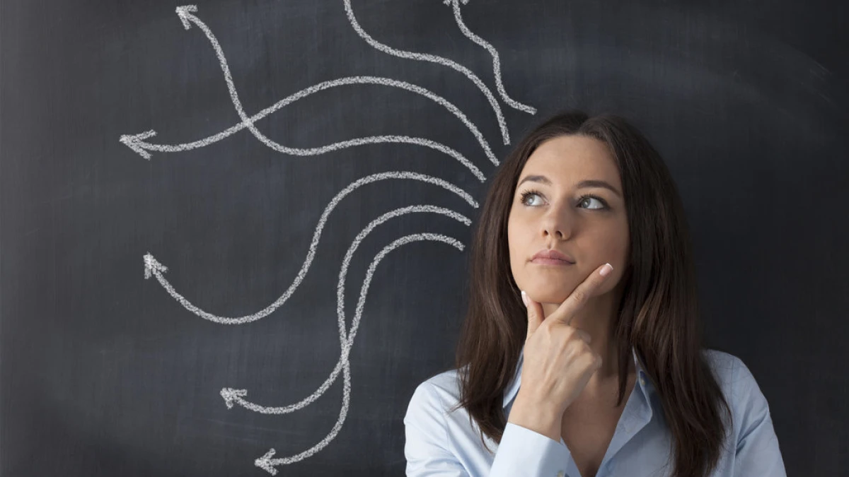 A woman touching her chin in front of a board with chalk-drawn arrows