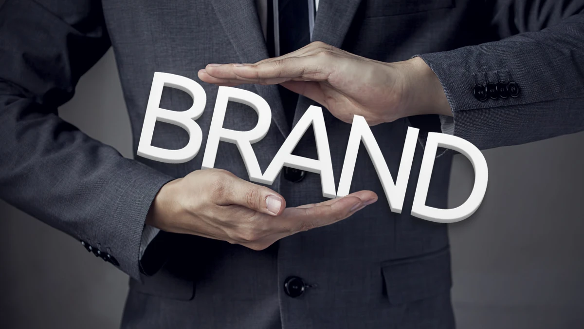 A person in a suit holding three-dimensional letters spelling BRAND