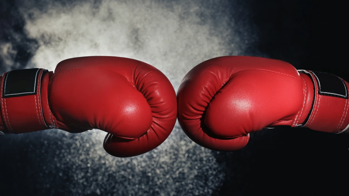 Two red boxing gloves touching against a dark background
