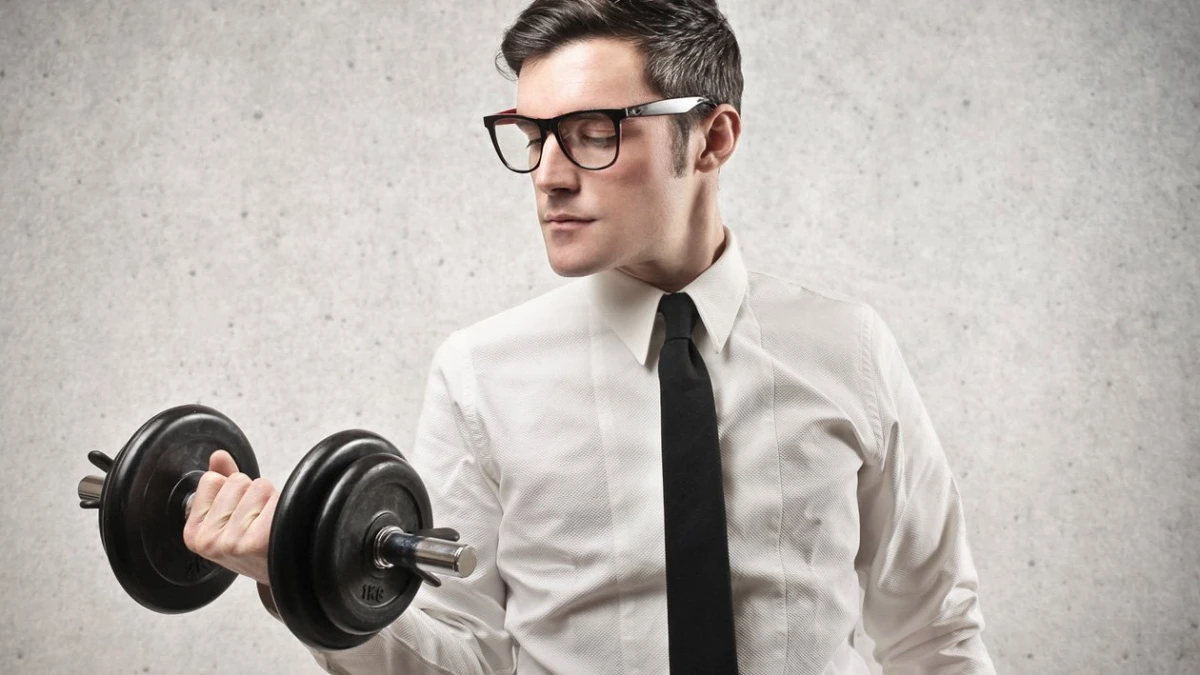A man in glasses, a white shirt and a black tie lifting a dumbbell