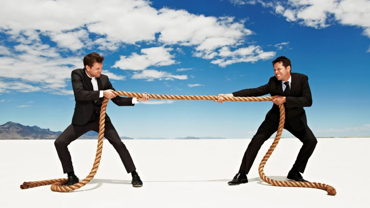 Two men in suits pulling opposite ends of a rope under a blue sky
