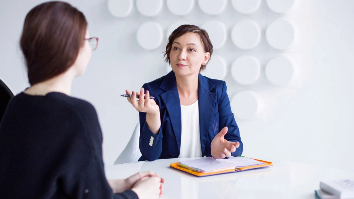 Two women talking at a table with an open folder of notes