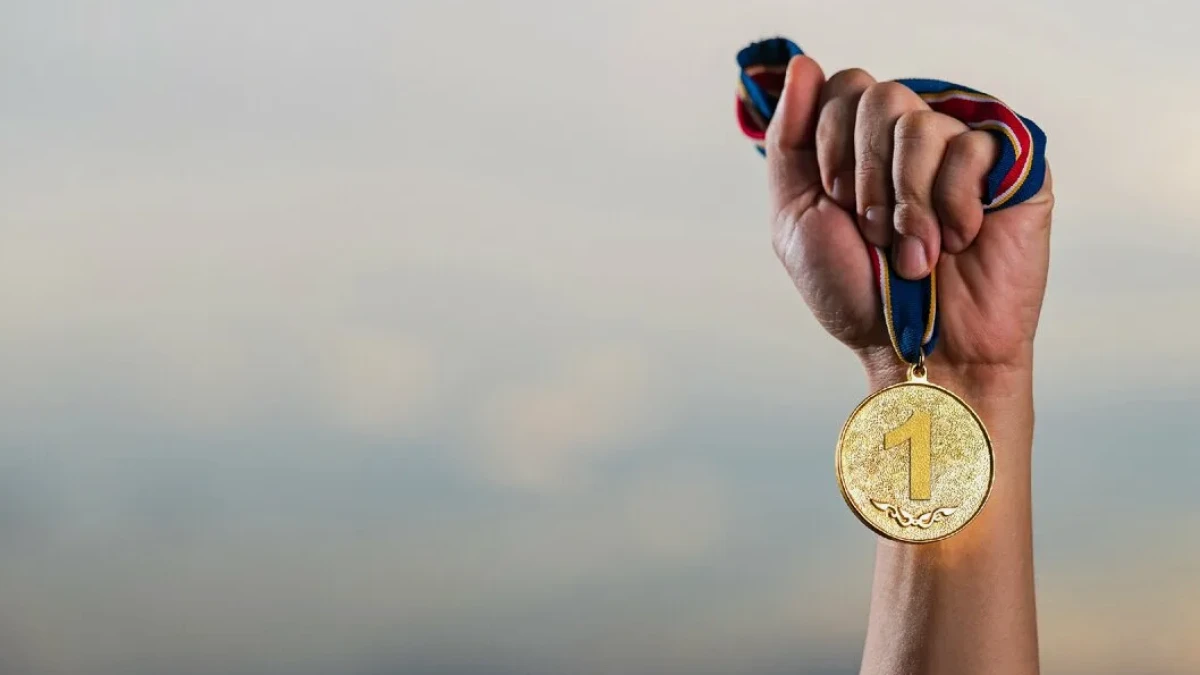 A hand holding a medal marked with the number one on a colourful ribbon