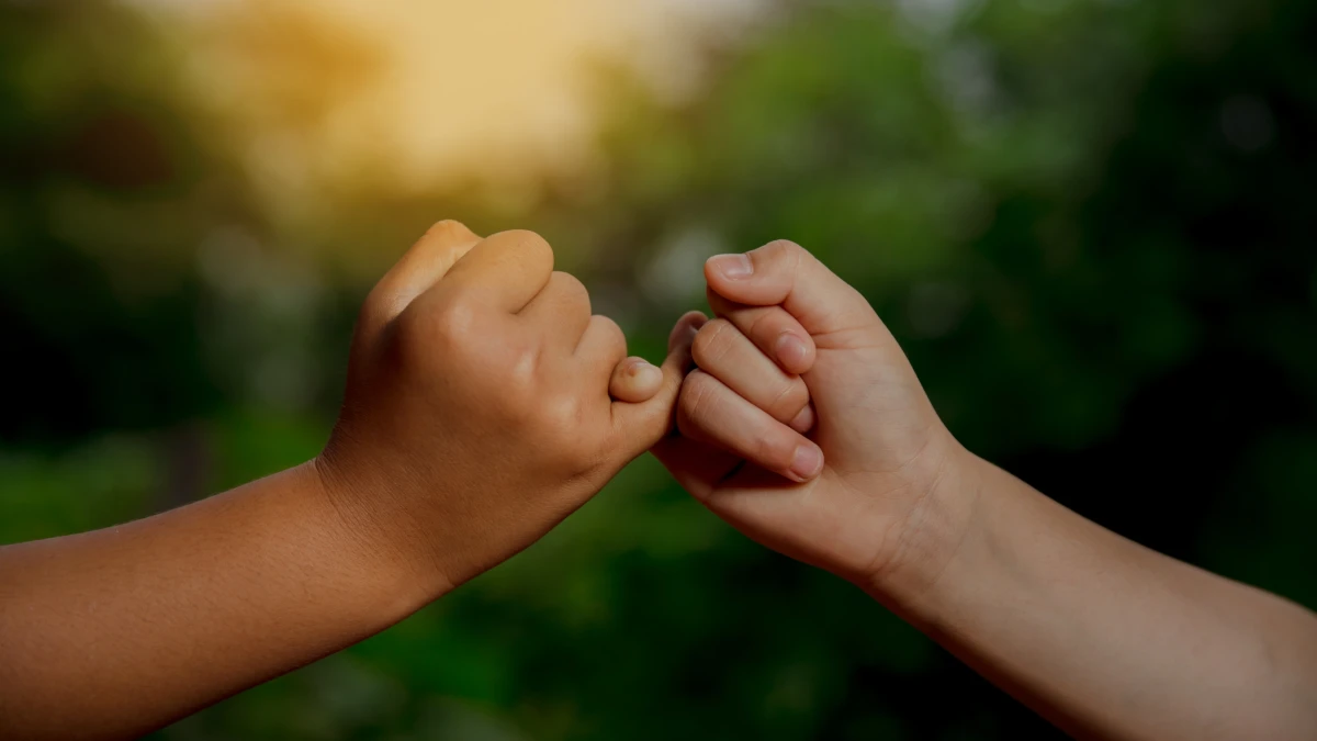Two hands with linked little fingers against a blurred green background
