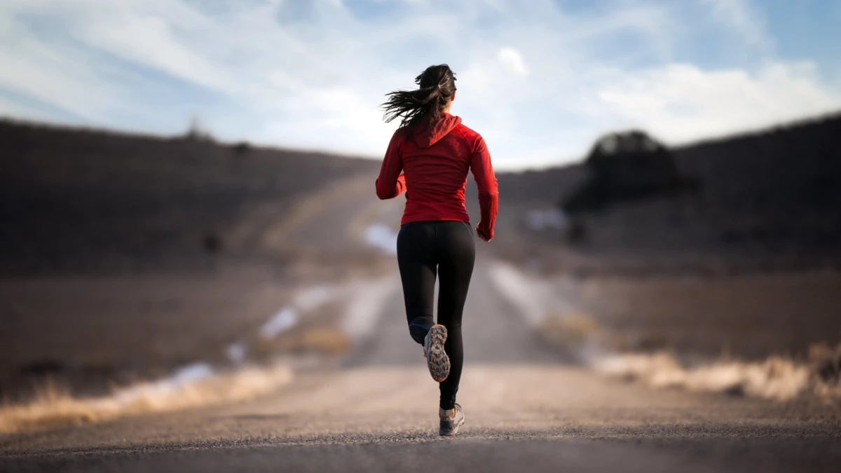 A woman in a red jacket running along a road between hills