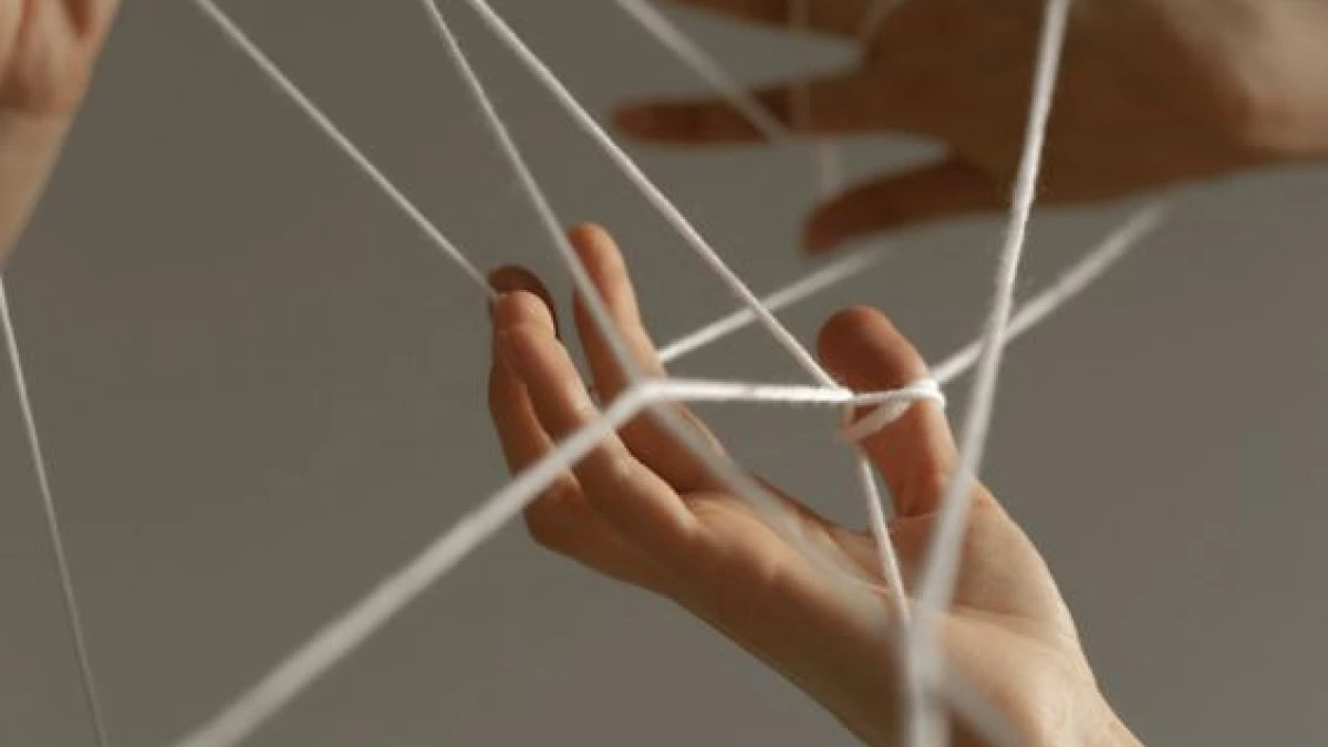Hands holding white threads stretched between the fingers
