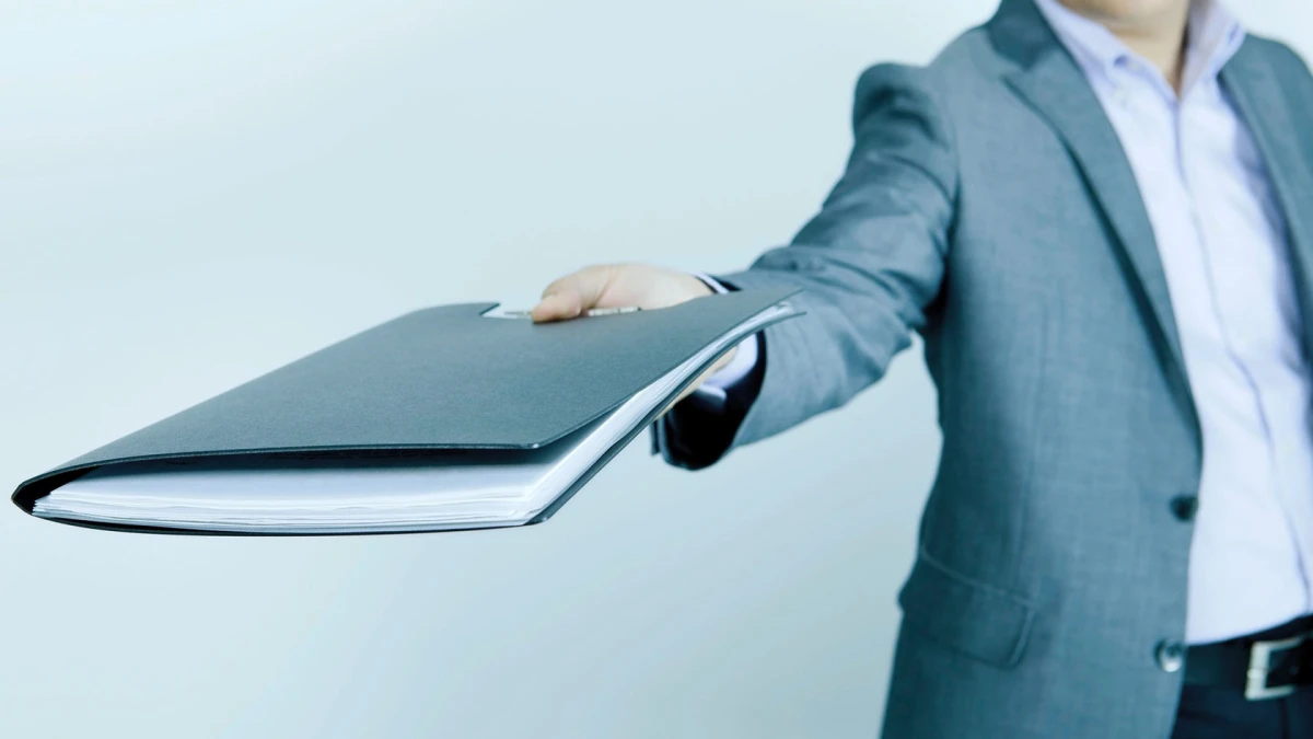 A person in a grey jacket holding out a folder of documents