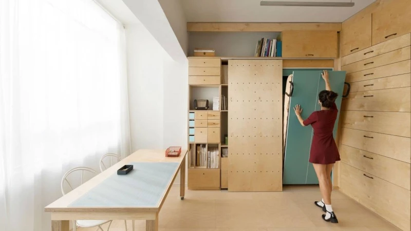 A woman beside built-in storage in a bright room with wooden furniture