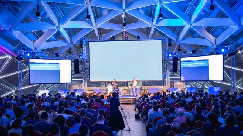 An audience seated in front of two speakers and large screens