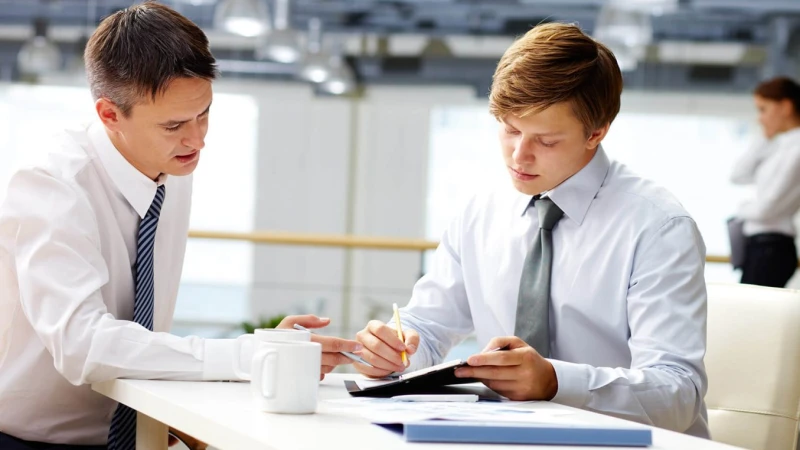 Two men discuss notes at a table in an office